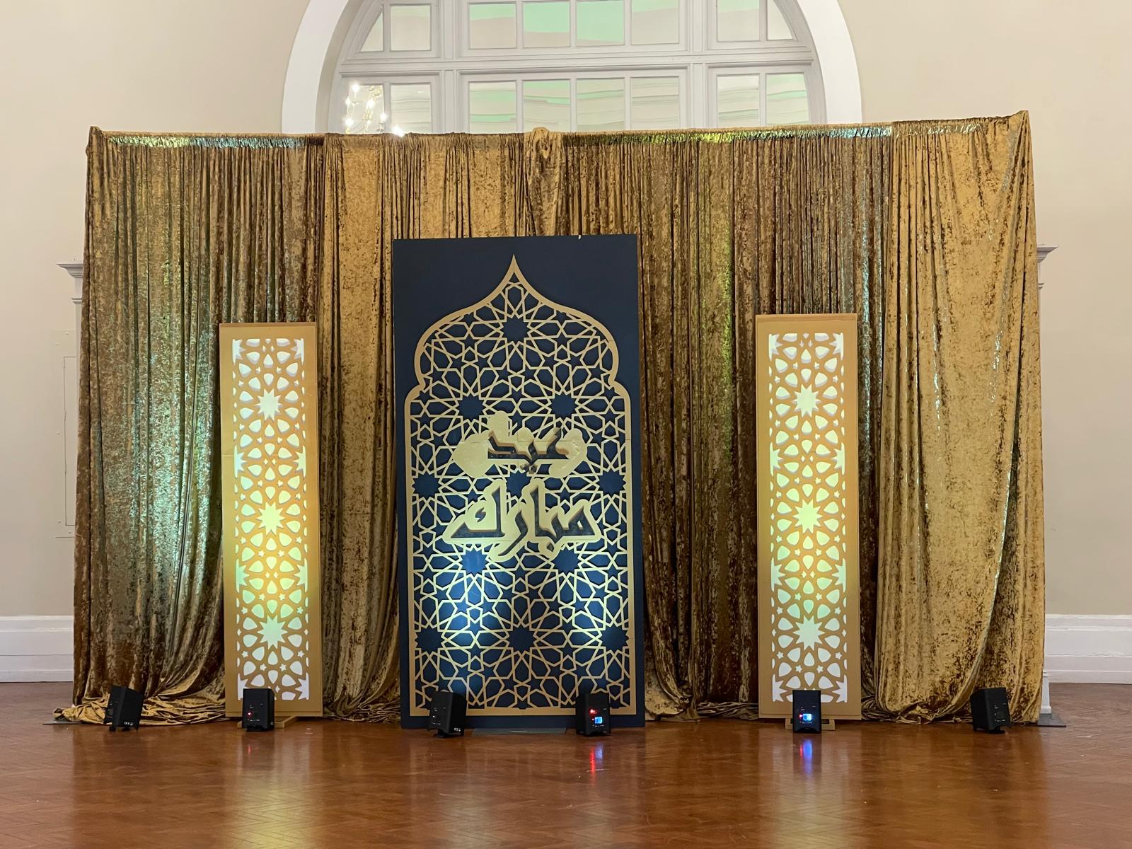 Gold arabesque backdrop with Eid Mubarak calligraphy and illuminated geometric panels — custom decor by Pixel N Sound Events